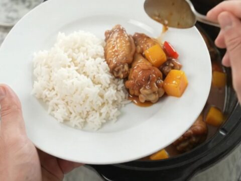Slow cooker mango teriyaki chicken wings in a black crockpot, glossy sauce, sesame seeds