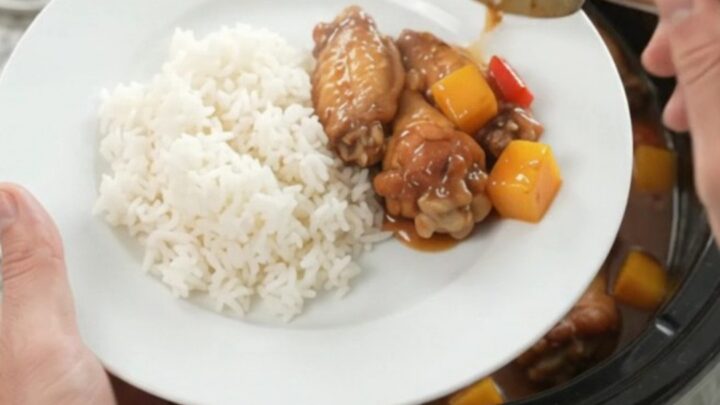 Slow cooker mango teriyaki chicken wings in a black crockpot, glossy sauce, sesame seeds