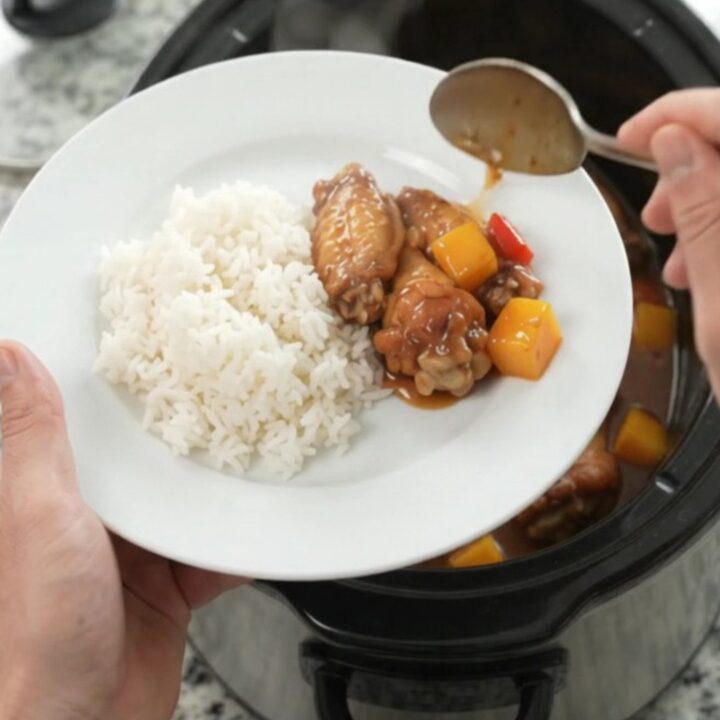 Slow cooker mango teriyaki chicken wings in a black crockpot, glossy sauce, sesame seeds