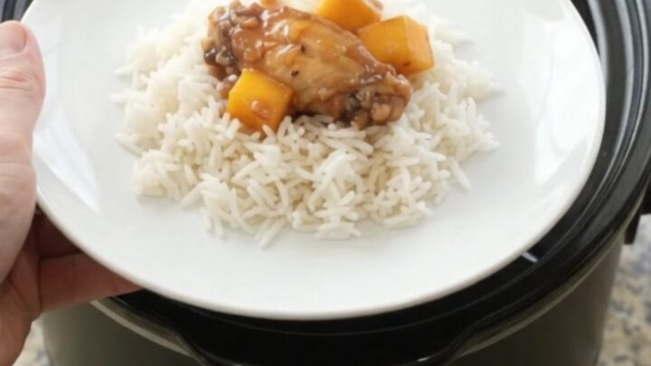 Sticky mango honey soy chicken wings in a slow cooker, glistening with sauce and garnished with mango cubes and red peppers.