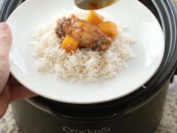 Sticky mango honey soy chicken wings in a slow cooker, glistening with sauce and garnished with mango cubes and red peppers.