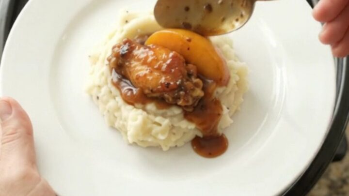 Sticky peach bourbon glazed chicken wings in a black crockpot with glossy sauce