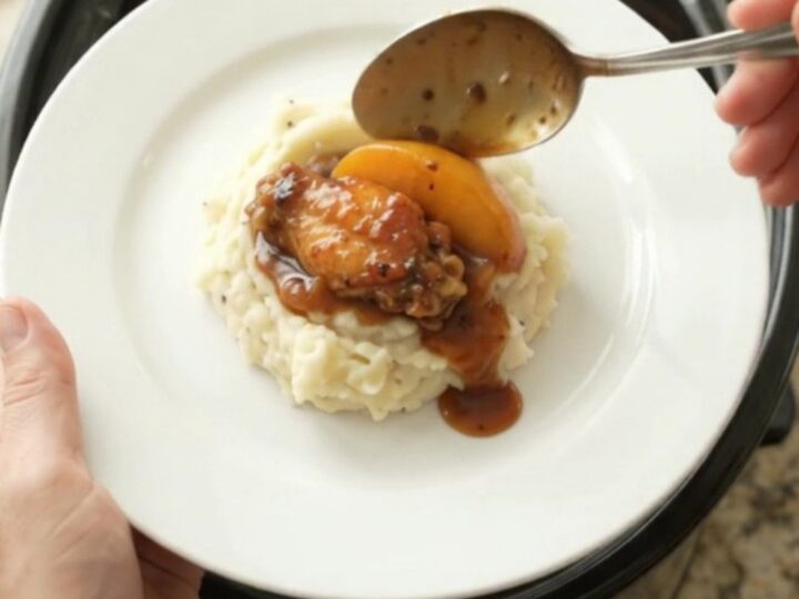 Sticky peach bourbon glazed chicken wings in a black crockpot with glossy sauce