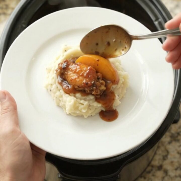 Sticky peach bourbon glazed chicken wings in a black crockpot with glossy sauce