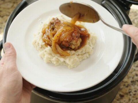 Sticky apricot bourbon glazed chicken wings in a black slow cooker with golden onion ribbons
