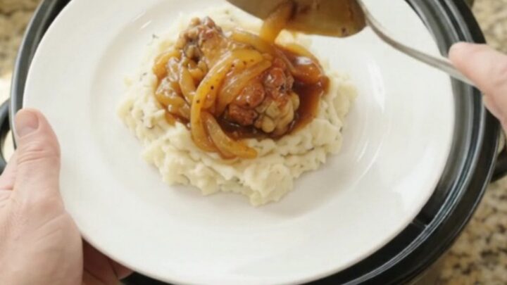 Sticky apricot bourbon glazed chicken wings in a black slow cooker with golden onion ribbons