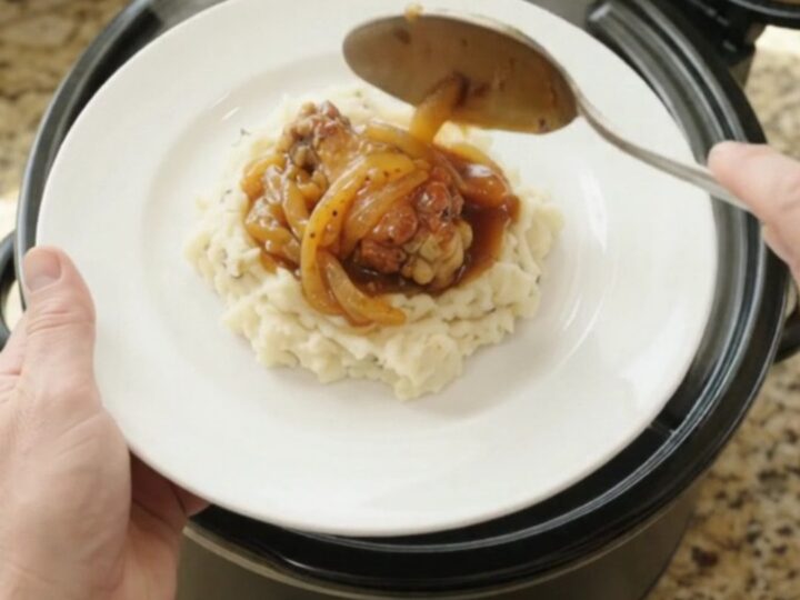 Sticky apricot bourbon glazed chicken wings in a black slow cooker with golden onion ribbons