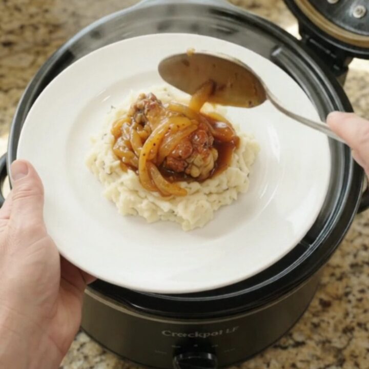 Sticky apricot bourbon glazed chicken wings in a black slow cooker with golden onion ribbons