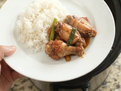 Sticky teriyaki chicken wings in a slow cooker, garnished with sesame seeds and scallions