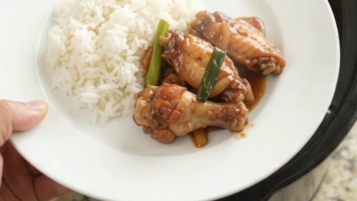 Sticky teriyaki chicken wings in a slow cooker, garnished with sesame seeds and scallions