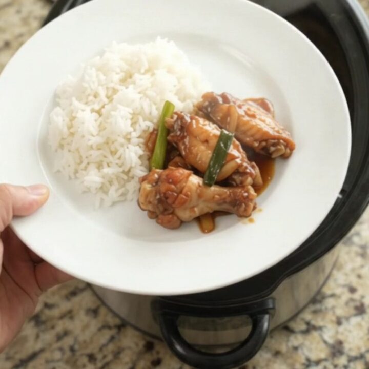 Sticky teriyaki chicken wings in a slow cooker, garnished with sesame seeds and scallions