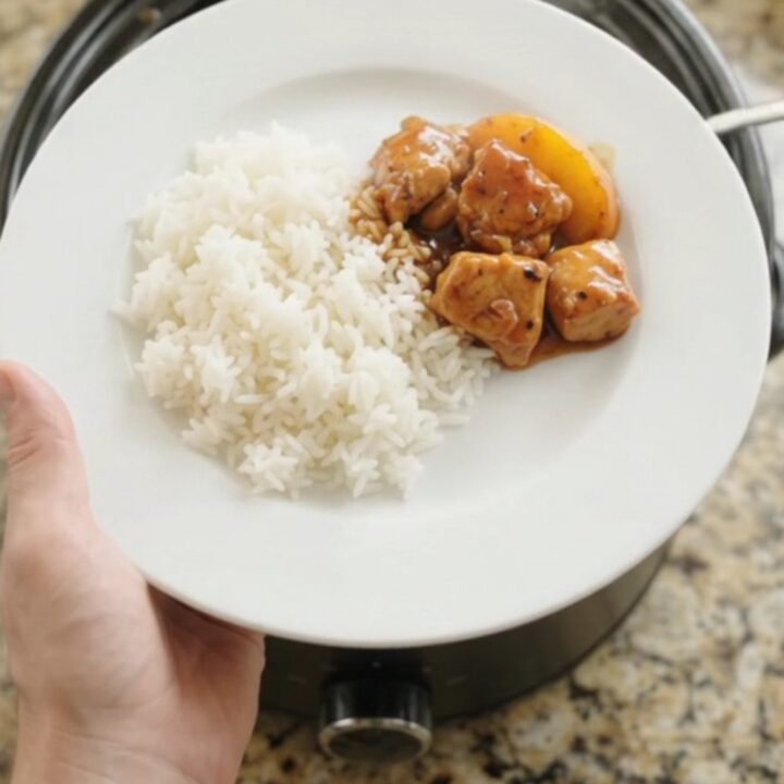 A slow cooker filled with glazed chicken and peach slices in hickory BBQ sauce