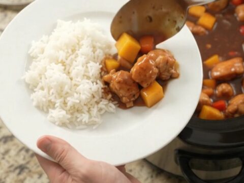 A bowl of mango hickory BBQ chicken bites with rice, garnished with fresh herbs