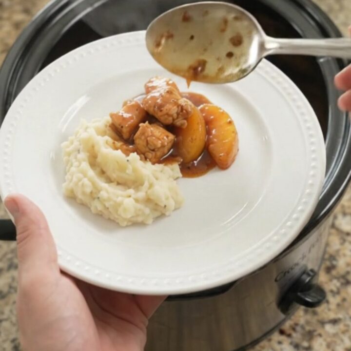 Glazed chicken bites and peach slices in a bubbling bourbon molasses sauce in a slow cooker