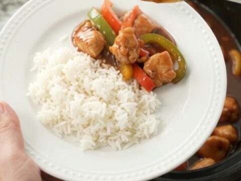 Slow-cooker hickory BBQ chicken bites with bell peppers in a black crockpot, coated in thick glaze.