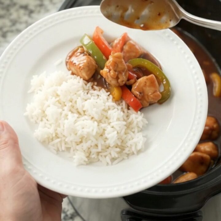 Slow-cooker hickory BBQ chicken bites with bell peppers in a black crockpot, coated in thick glaze.