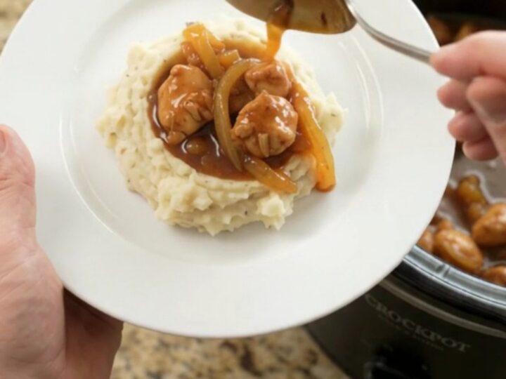 A slow cooker filled with glazed chicken bites in sticky apricot bourbon sauce, topped with caramelized onion ribbons.