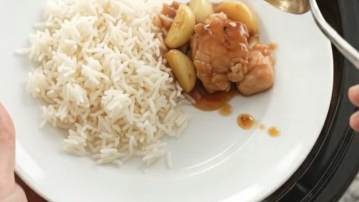 Honey garlic chicken bites in a slow cooker with whole garlic cloves and scallions, glistening in a sticky amber sauce.