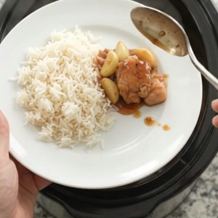 Honey garlic chicken bites in a slow cooker with whole garlic cloves and scallions, glistening in a sticky amber sauce.