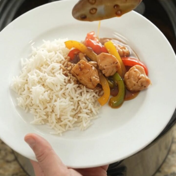 Slow cooker honey soy chicken bites with bell peppers and onions, glazed and steaming in the crock