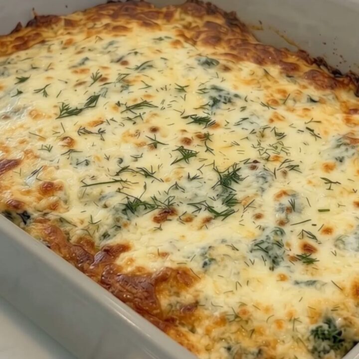 A bubbly golden-brown Greek chicken and broccoli bake in a grey rectangular baking dish on a kitchen counter