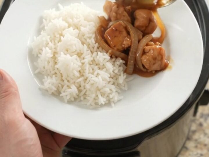 Crockpot full of glazed chicken bites and caramelized onions with steam rising