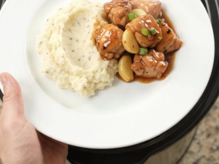 Slow cooker filled with glazed chicken bites, garlic cloves, and scallions in a dark bourbon sauce.