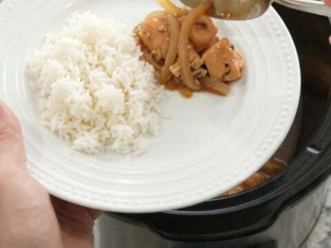 Slow cooker teriyaki chicken bites with caramelized Vidalia onions and sesame seeds in a black crockpot.