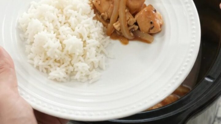 Slow cooker teriyaki chicken bites with caramelized Vidalia onions and sesame seeds in a black crockpot.