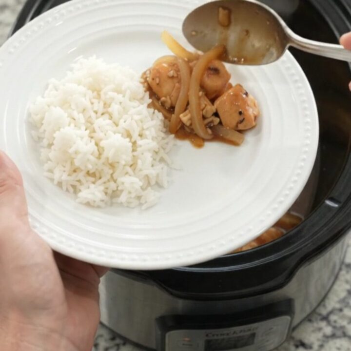 Slow cooker teriyaki chicken bites with caramelized Vidalia onions and sesame seeds in a black crockpot.