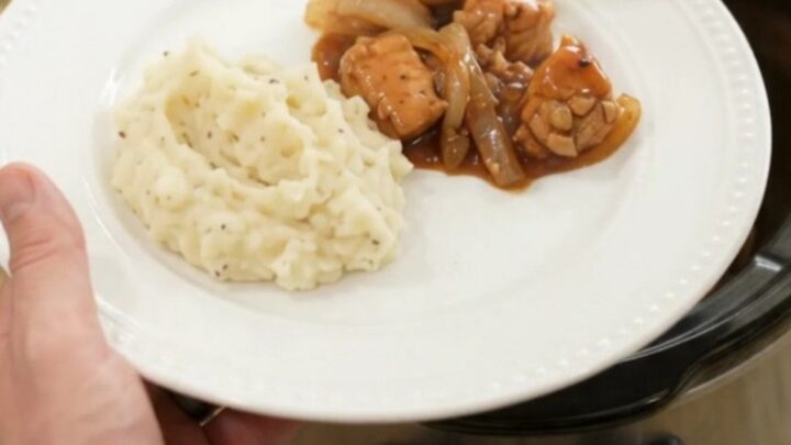 Slow cooker full of glazed chicken bites and caramelized onions with a spoon lifting a portion