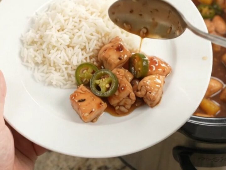 A slow cooker filled with glazed honey soy chicken bites, pineapple, and jalapeños, with steam rising.