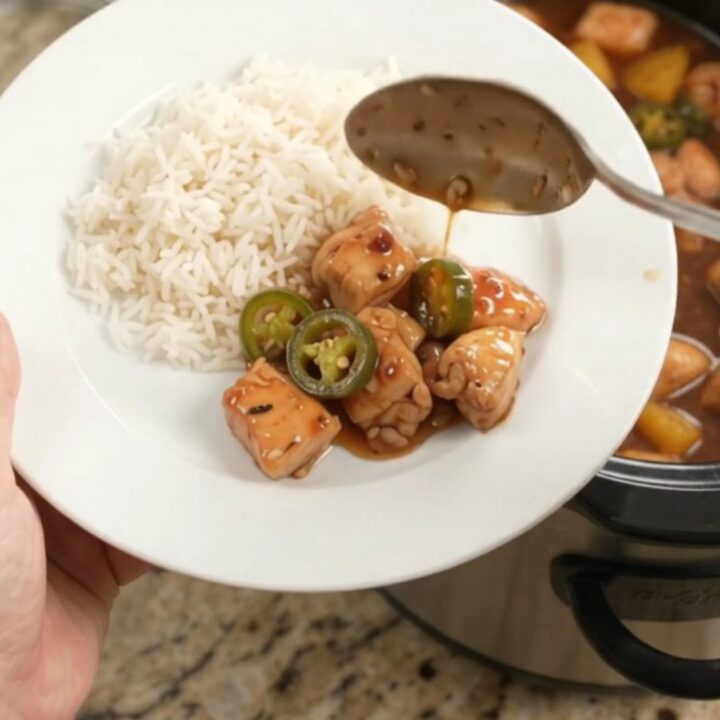A slow cooker filled with glazed honey soy chicken bites, pineapple, and jalapeños, with steam rising.