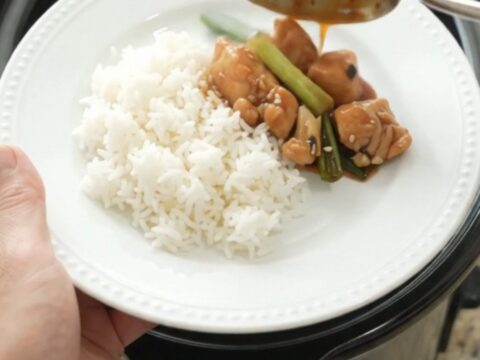 Slow cooker ginger scallion teriyaki chicken bites in a black ceramic pot, glossy glaze on the chicken