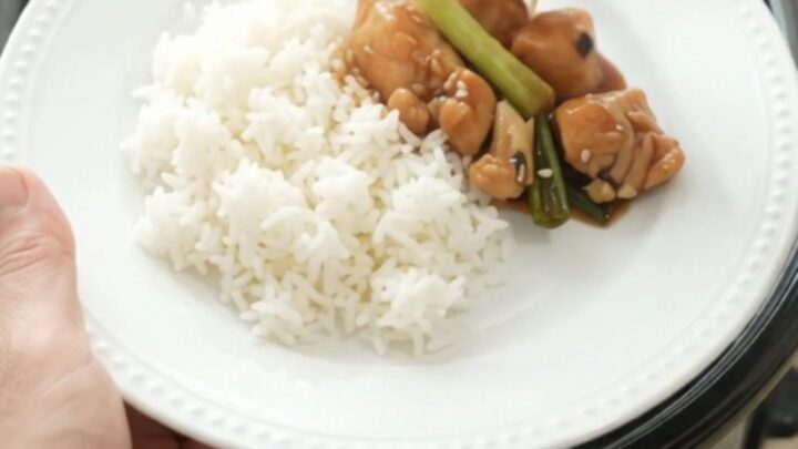 Slow cooker ginger scallion teriyaki chicken bites in a black ceramic pot, glossy glaze on the chicken