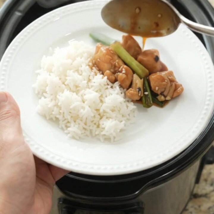Slow cooker ginger scallion teriyaki chicken bites in a black ceramic pot, glossy glaze on the chicken