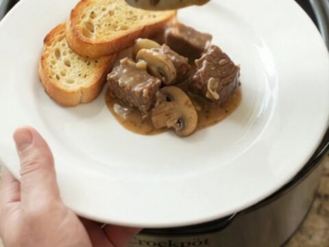 Gruyère Cream Mushroom Beef Bites in a black Crockpot, bubbling with cheese sauce