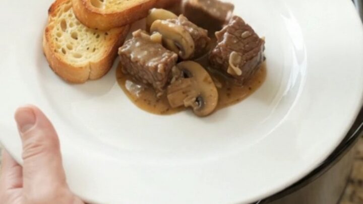 Gruyère Cream Mushroom Beef Bites in a black Crockpot, bubbling with cheese sauce