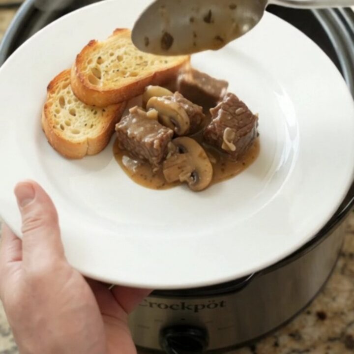 Gruyère Cream Mushroom Beef Bites in a black Crockpot, bubbling with cheese sauce