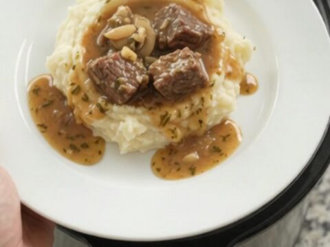 Slow cooker cowboy butter mushroom beef bites in a black crockpot with a spoon lifting a bite.