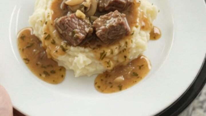 Slow cooker cowboy butter mushroom beef bites in a black crockpot with a spoon lifting a bite.