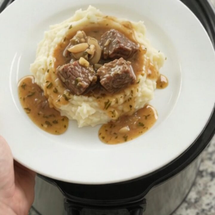 Slow cooker cowboy butter mushroom beef bites in a black crockpot with a spoon lifting a bite.