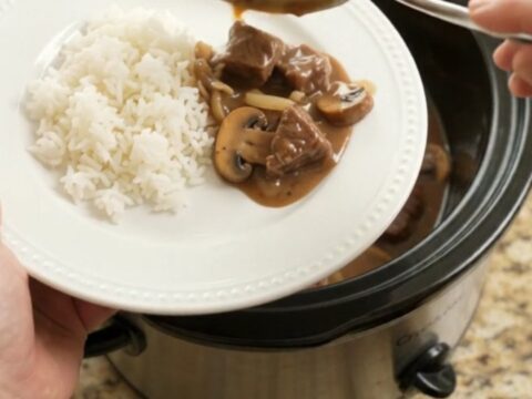 A slow cooker filled with tender beef bites in a rich bourbon-mushroom gravy, with steam rising.
