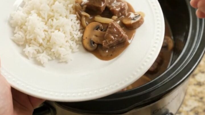 A slow cooker filled with tender beef bites in a rich bourbon-mushroom gravy, with steam rising.