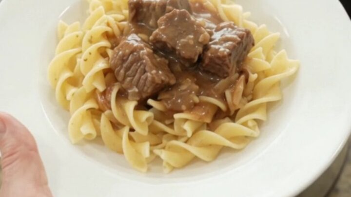 Slow cooker sour cream garlic potato beef bites in a black crock, topped with gravy, ready to serve.