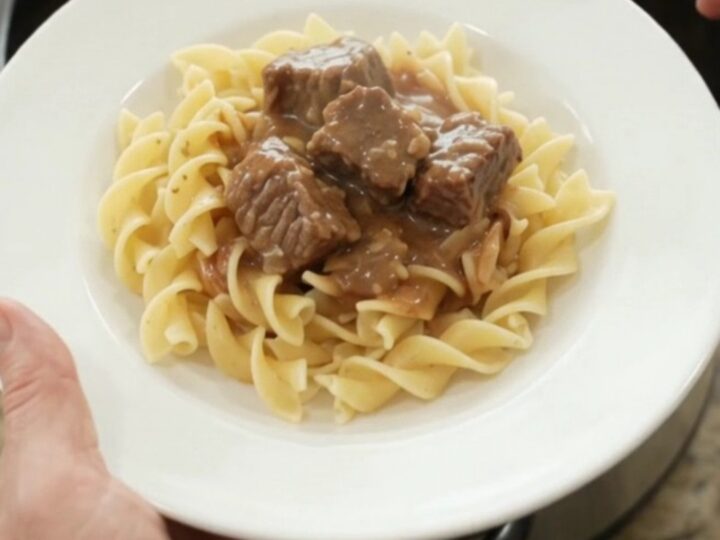 Slow cooker sour cream garlic potato beef bites in a black crock, topped with gravy, ready to serve.