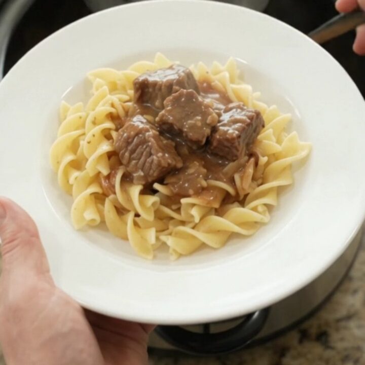 Slow cooker sour cream garlic potato beef bites in a black crock, topped with gravy, ready to serve.