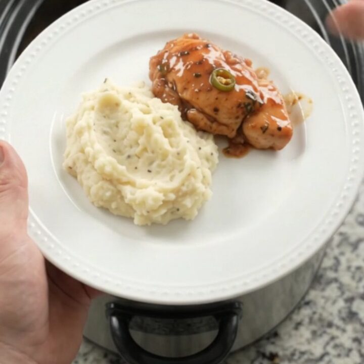 Slow cooker chicken bites in bourbon glaze with pineapple and jalapeños, served in a black crockpot.