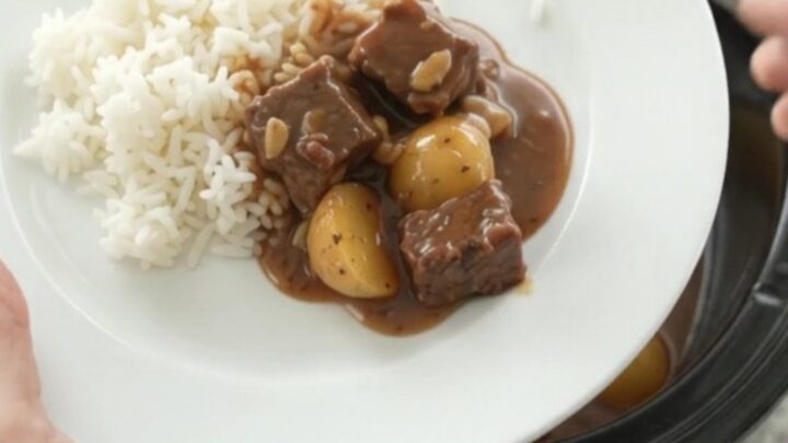 Slow cooker bourbon gravy beef bites with potatoes and garlic, served in a black crockpot