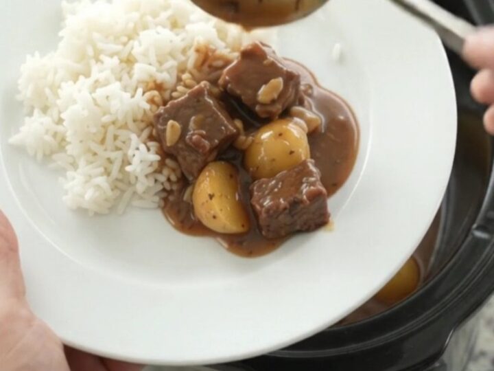 Slow cooker bourbon gravy beef bites with potatoes and garlic, served in a black crockpot